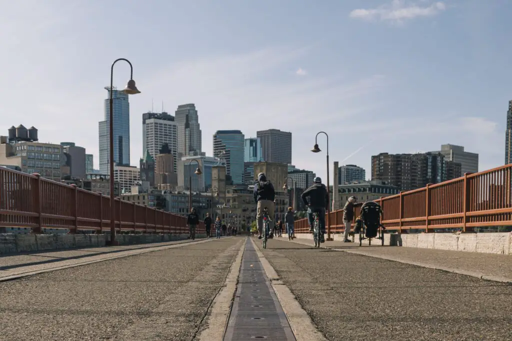 Pedestrian bridge with walkers and bikers and the Minneapolis skyline in the background.