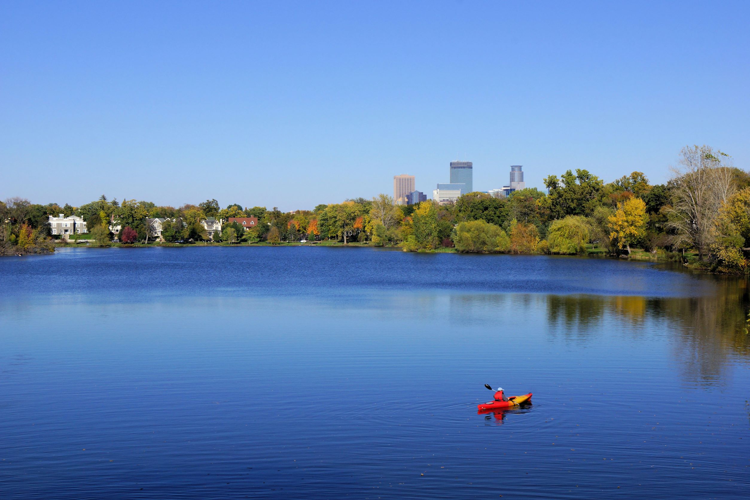 Lake surrounded by trees with Minneapolis skyline in the back