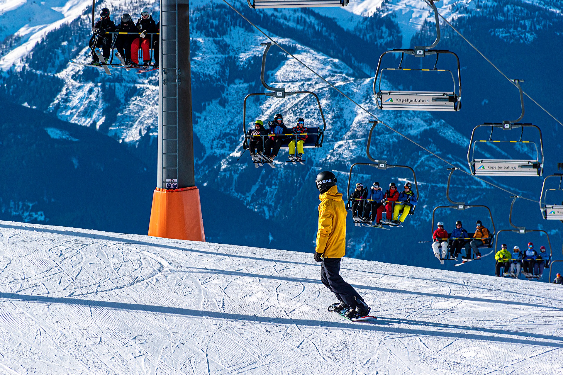 Groups of people riding a ski lift with a snowboarder going down the mountain